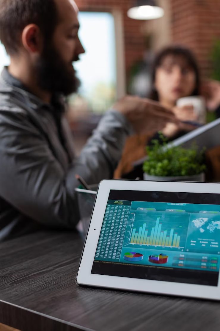 tablet-computer-with-company-statistics-screen-standing-table-startup-office-millennial-multiethnic-businesspeople-discussing-marketing-strategy-working-business-collaboration